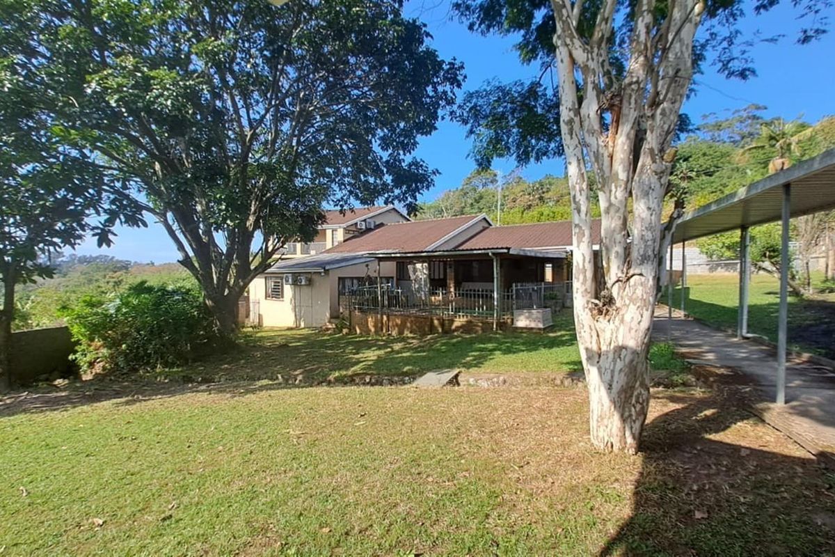 A view of the rear exterior of the property, featuring a covered patio area, established garden, and a paved walkway.