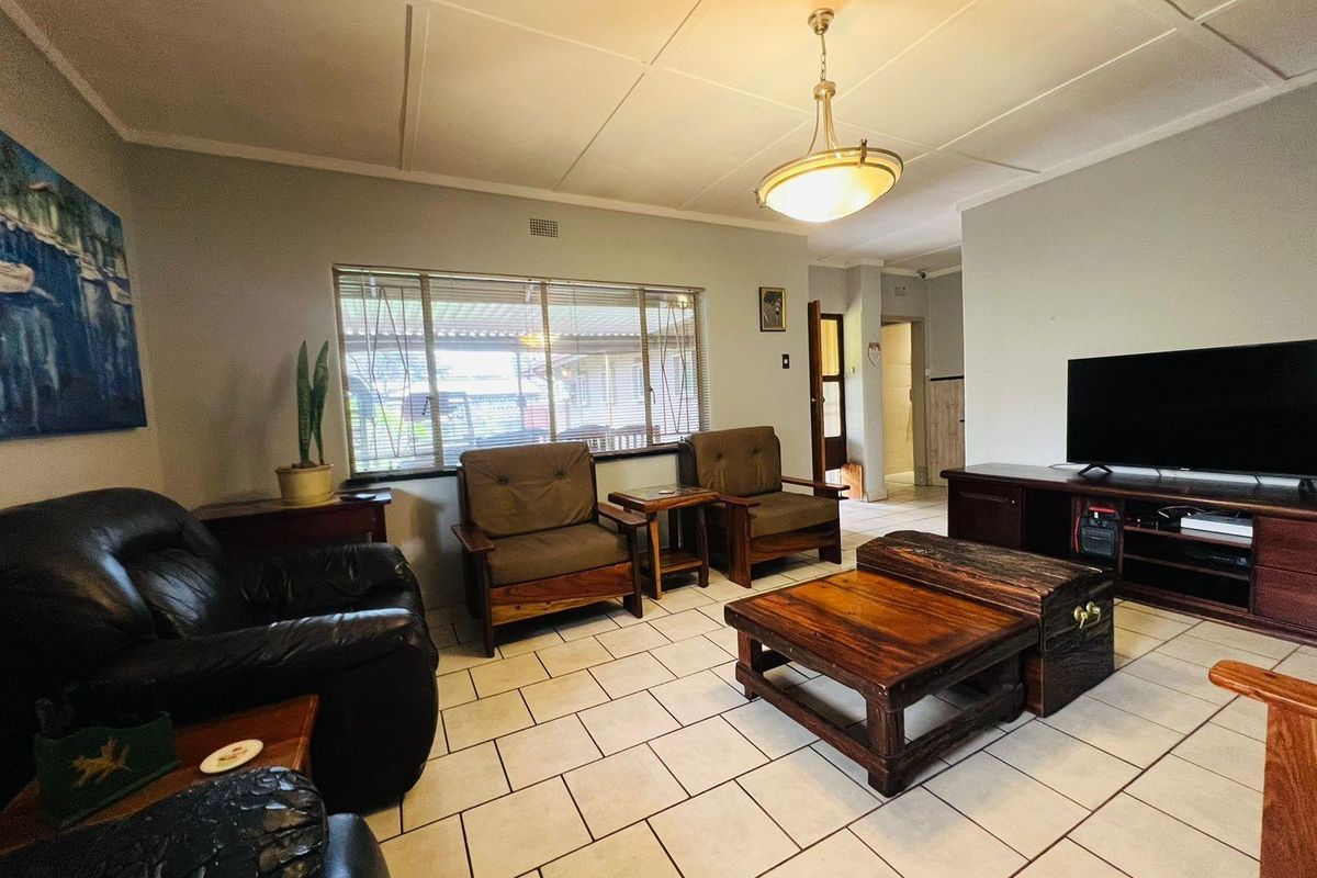 A spacious living room featuring tiled flooring, a central pendant light fixture, and large windows allowing natural light into the living area.