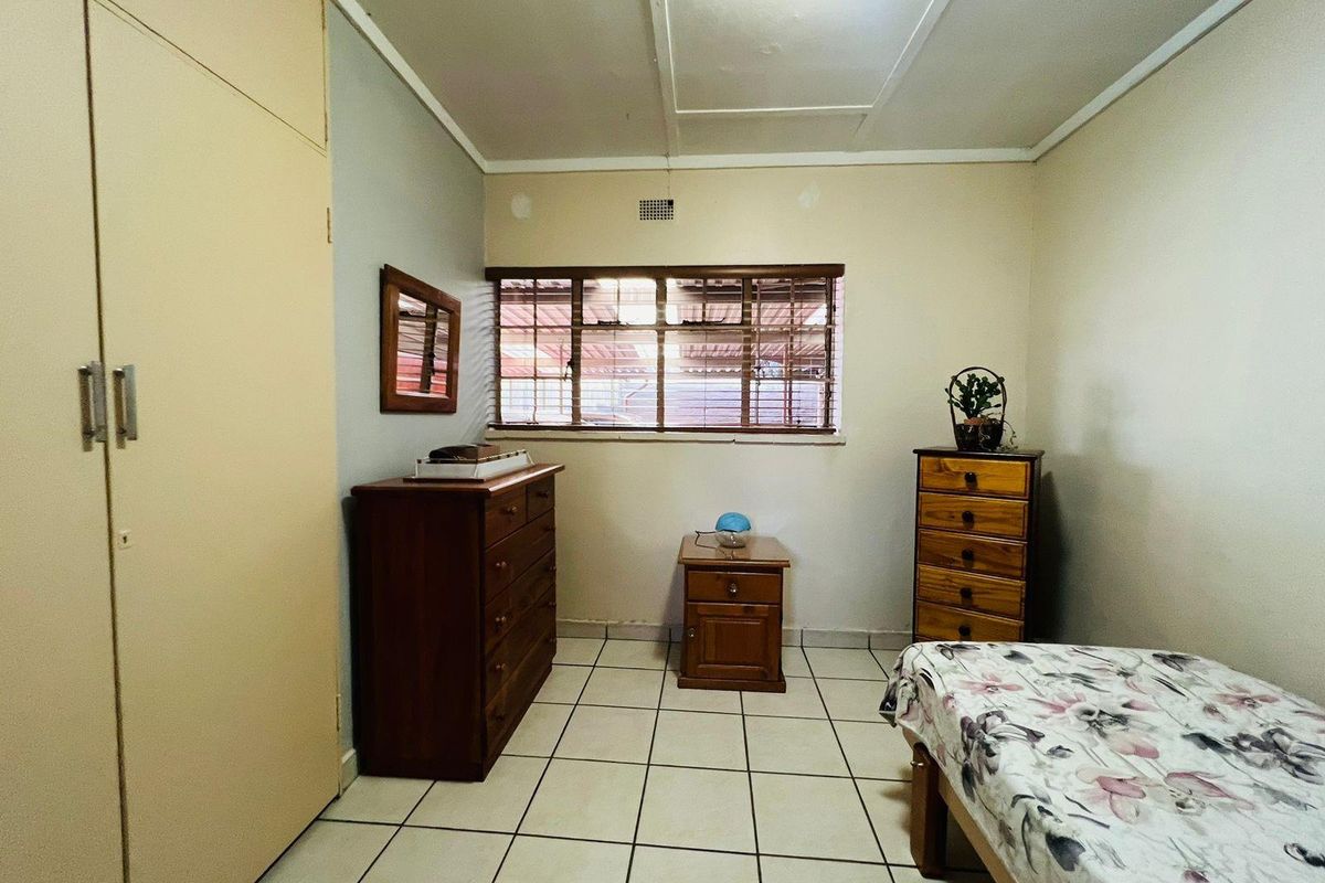 A functional bedroom featuring built-in cupboards, tiled flooring, and a window with horizontal blinds, offering a neutral space ready for personalization.