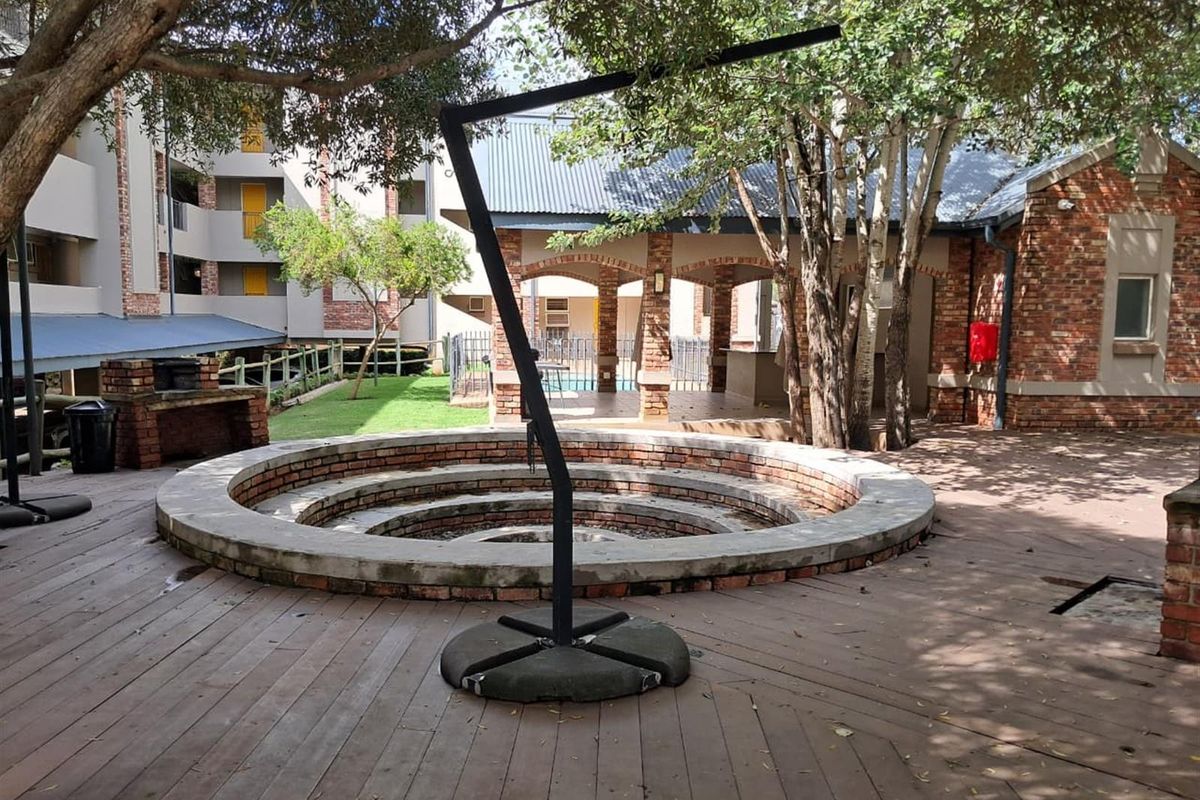 Outdoor communal area featuring a circular sunken brick fire pit, timber decking, and a covered patio space within a landscaped apartment complex.