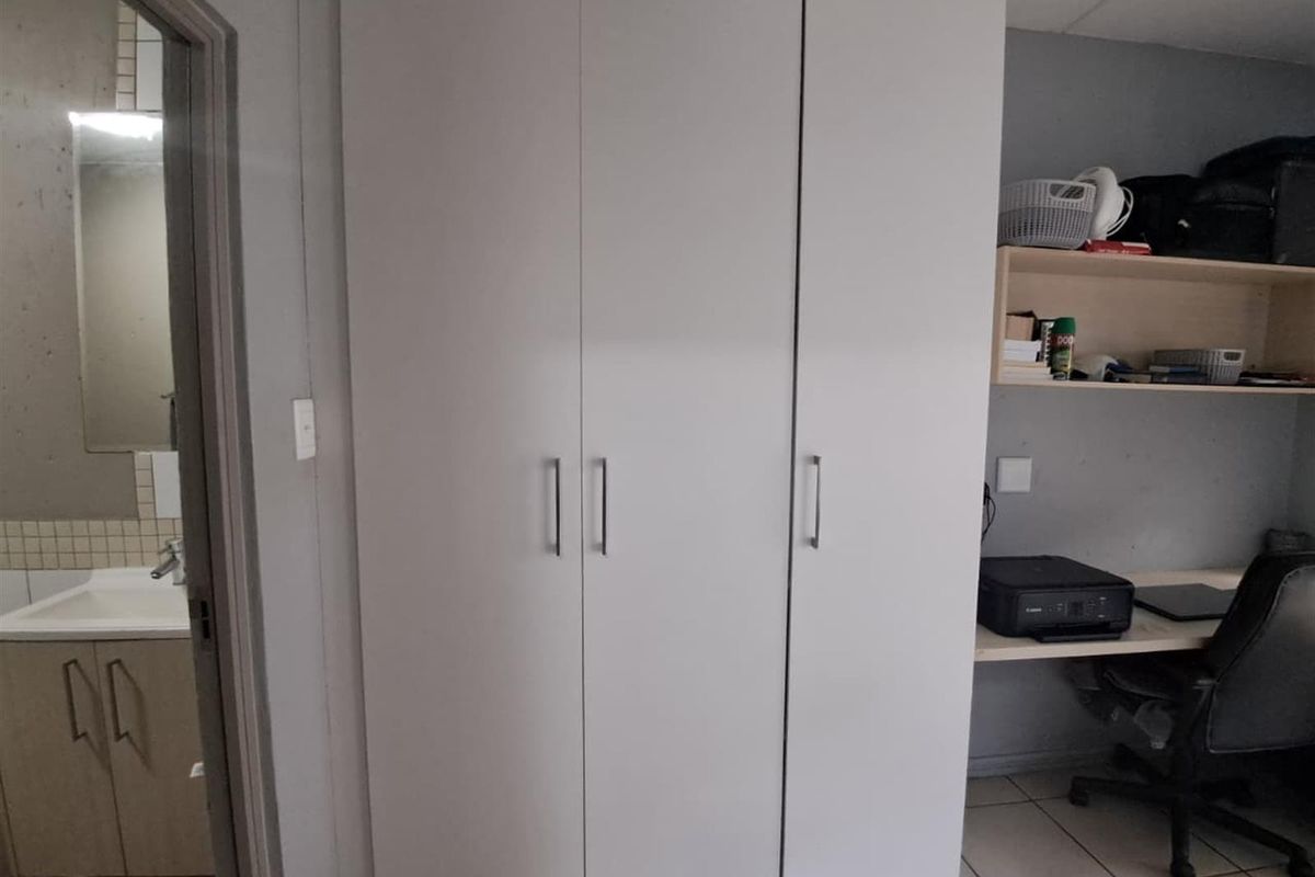 A bedroom featuring a built-in wardrobe and a built-in desk area, with an adjacent view into a bathroom with a vanity.