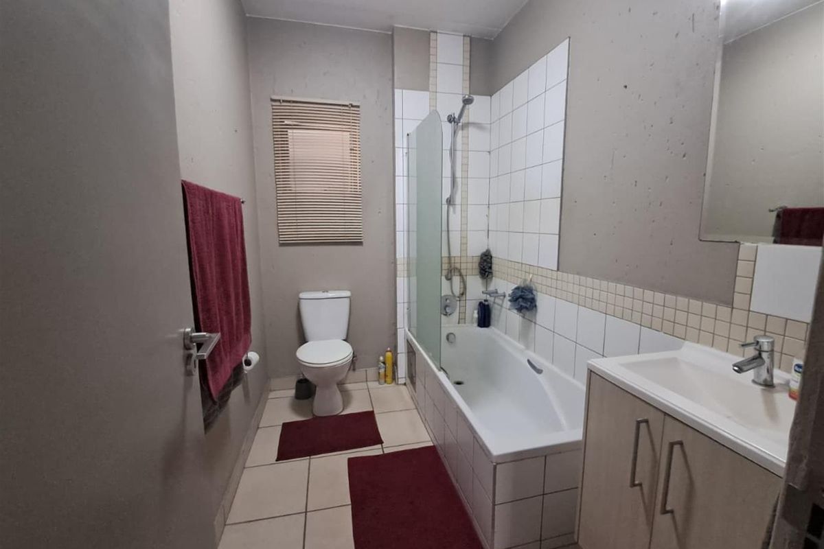 A functional bathroom featuring a bathtub with a shower mixer, a vanity basin, and a toilet, finished with tiled flooring and partial wall tiling.