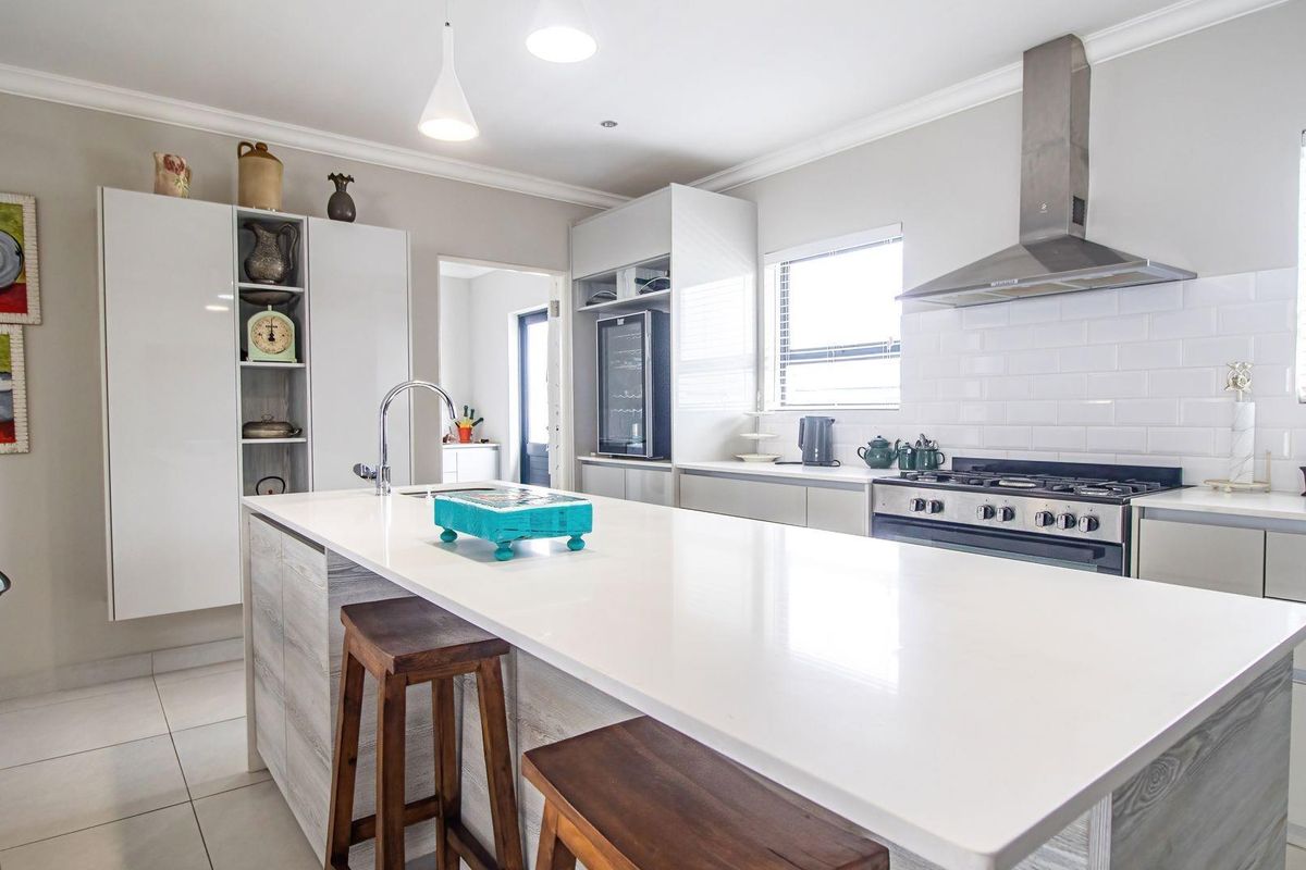 Modern kitchen featuring a large central island with stone countertop, gas stove, stainless steel extractor fan, and subway tile backsplash.