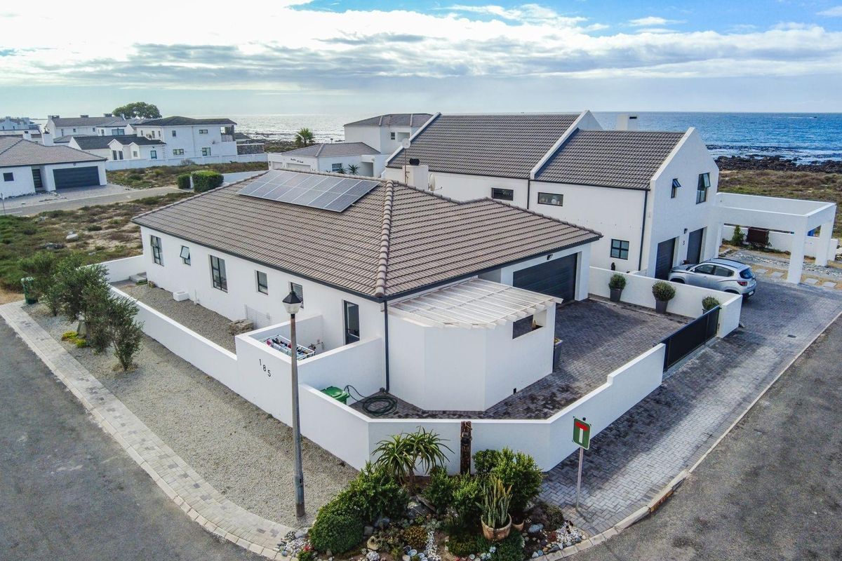Aerial view of a modern coastal residence featuring a tiled roof, solar panels, paved driveway, and secure perimeter walling in a quiet estate setting.