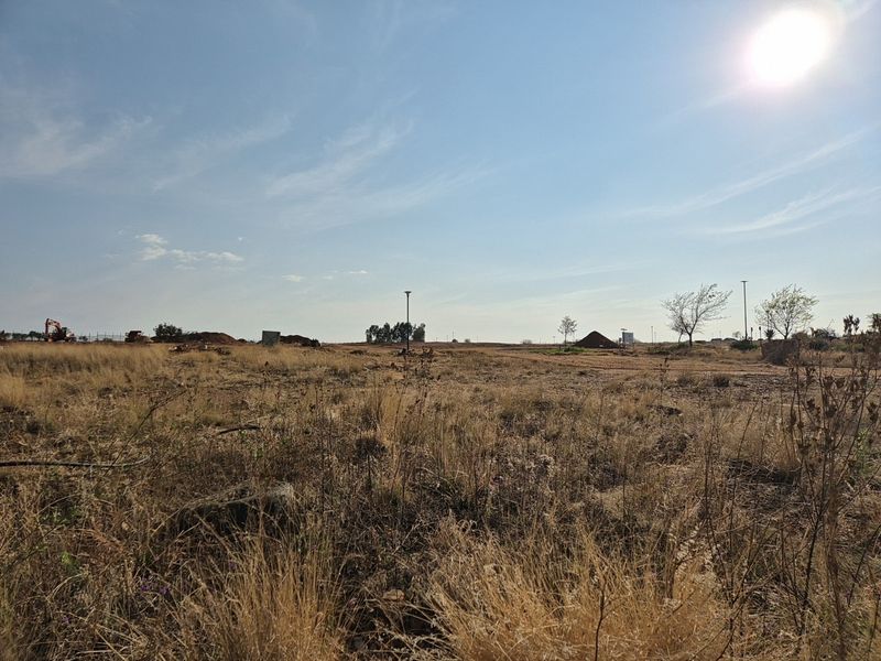 A wide-angle view of a vacant residential plot featuring dry grass, level terrain, and existing street lighting infrastructure.
