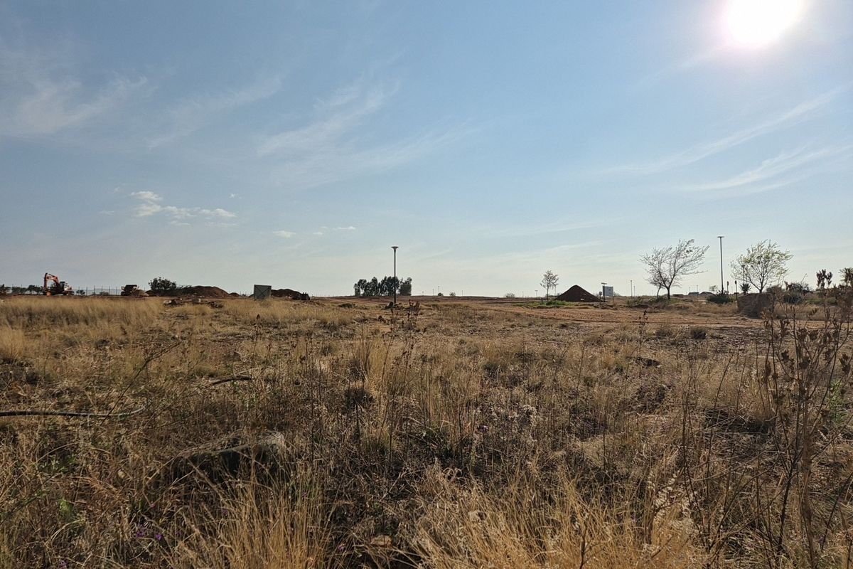 A wide-angle view of a vacant residential plot featuring dry grass, level terrain, and existing street lighting infrastructure.