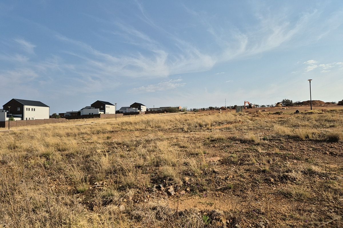 A view of a vacant residential plot featuring dry grass and surrounding neighborhood development.