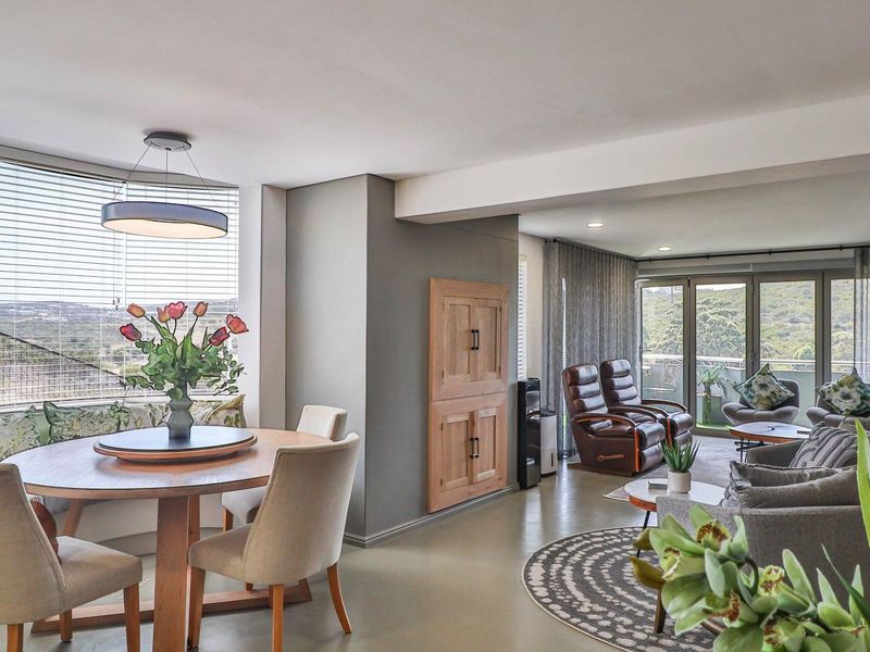An open-plan living and dining area featuring large windows, built-in bench seating, and seamless access to an outdoor balcony with scenic views.