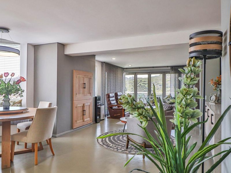 An open-plan living and dining area featuring smooth flooring, recessed lighting, and large glass sliding doors leading to an outdoor balcony with scenic views.
