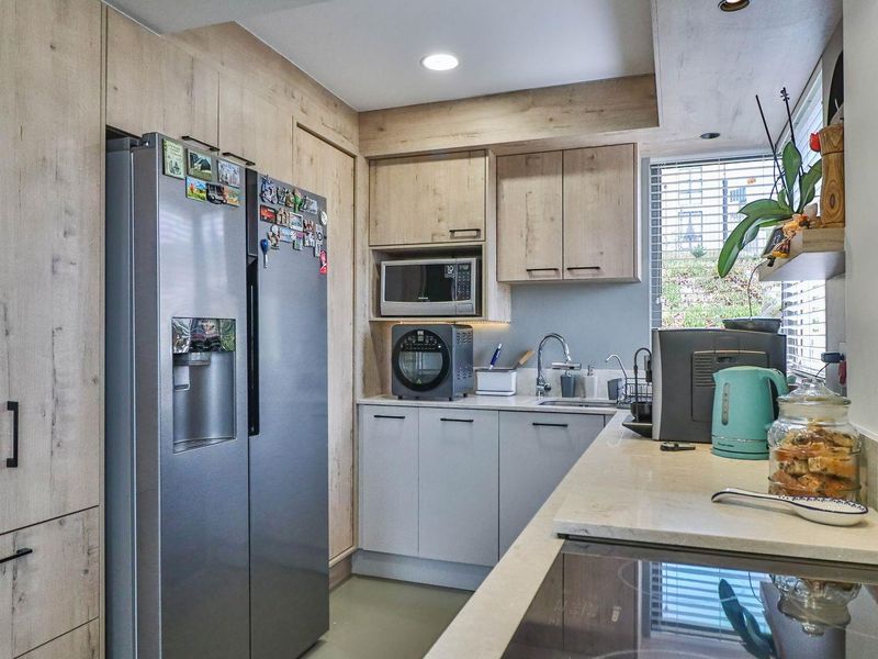A modern kitchen featuring light wood-grain cabinetry, stone countertops, a built-in microwave, and a stainless steel sink with a window view.