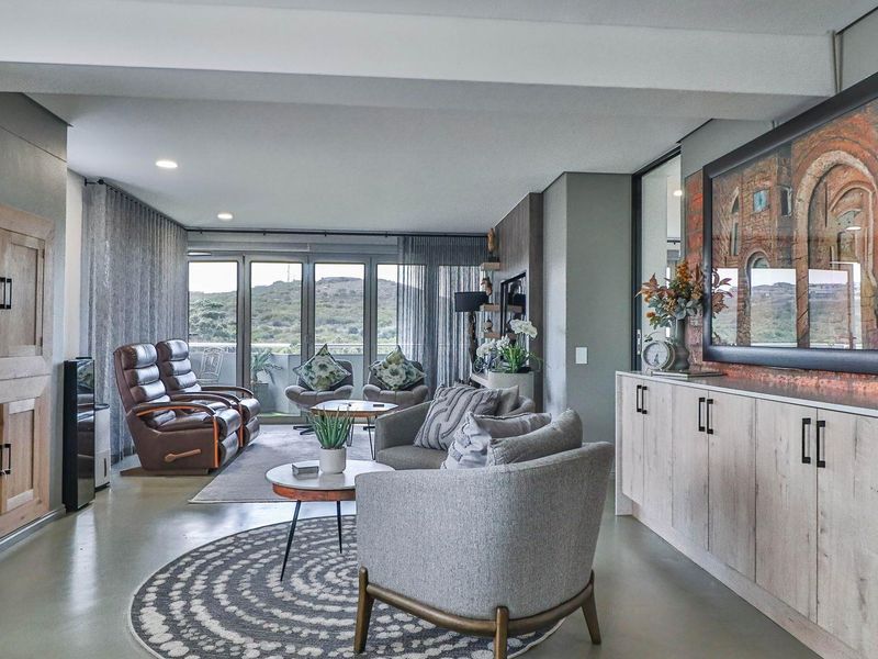 Spacious open-plan living area featuring polished concrete floors, a striking exposed brick feature wall, and large sliding doors leading to a balcony with scenic views.