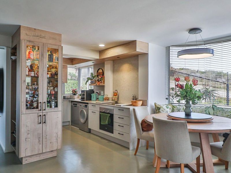 Modern open-plan kitchen and dining area featuring light wood cabinetry, integrated appliances, and a built-in display cabinet with glass shelving.