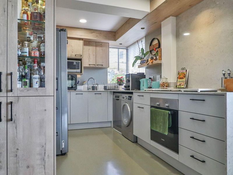Modern kitchen featuring light-toned cabinetry, integrated oven, built-in microwave, and sleek stone-look splashback with recessed lighting.