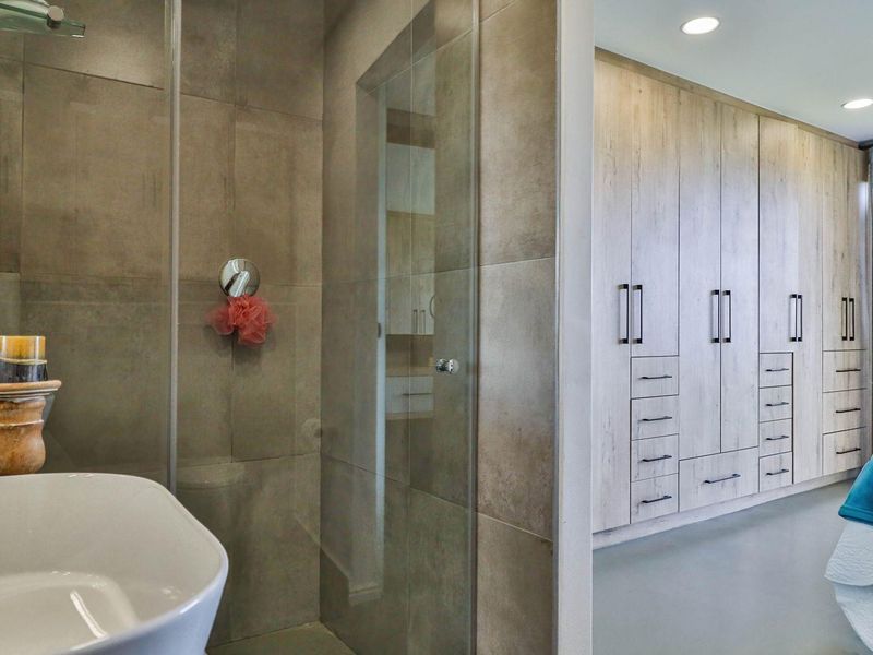 A modern bedroom featuring extensive built-in wooden cabinetry and an en-suite bathroom with a glass-enclosed shower and tiled finishes.