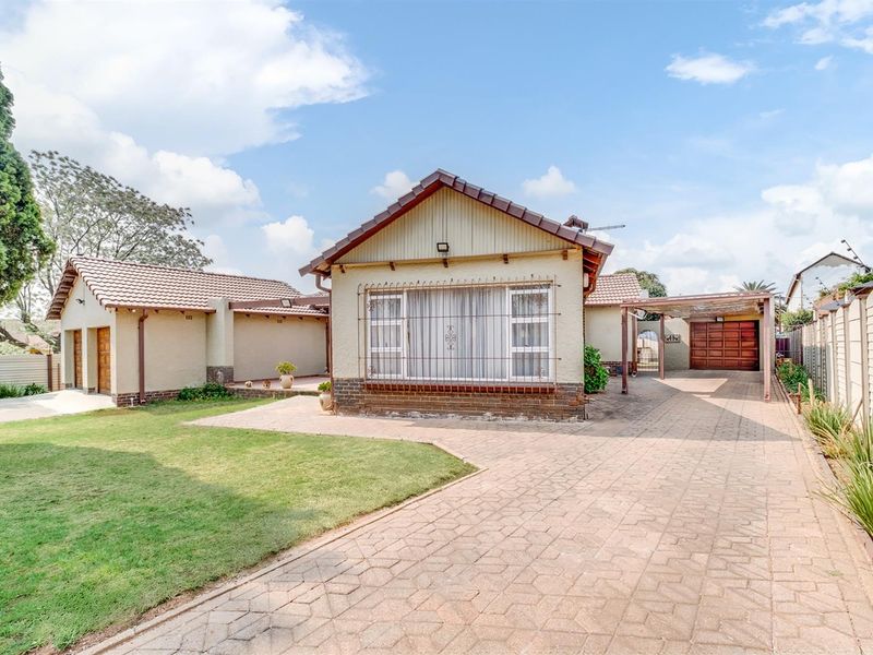 Front view of a well-maintained house featuring a paved driveway, carport, garage, and a neat front garden with established boundary walls.
