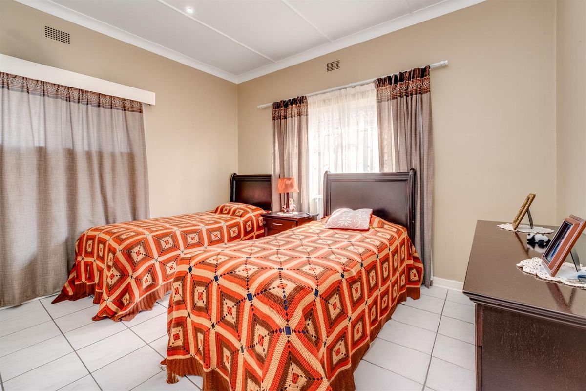 A well-maintained bedroom featuring tiled flooring, neutral wall tones, and dual windows with fitted curtain rails.