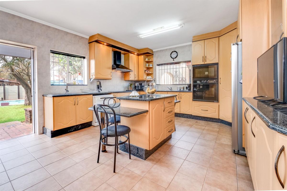 Spacious kitchen featuring light wood cabinetry, granite countertops, a central island, and built-in appliances, with direct access to the outdoor patio area.