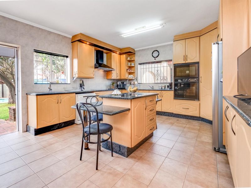 Spacious kitchen featuring light wood cabinetry, granite countertops, a central island, and built-in appliances, with direct access to the outdoor patio area.