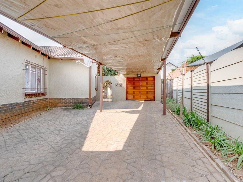 A paved driveway featuring a covered carport and a wooden garage door, enclosed by a precast concrete boundary wall.