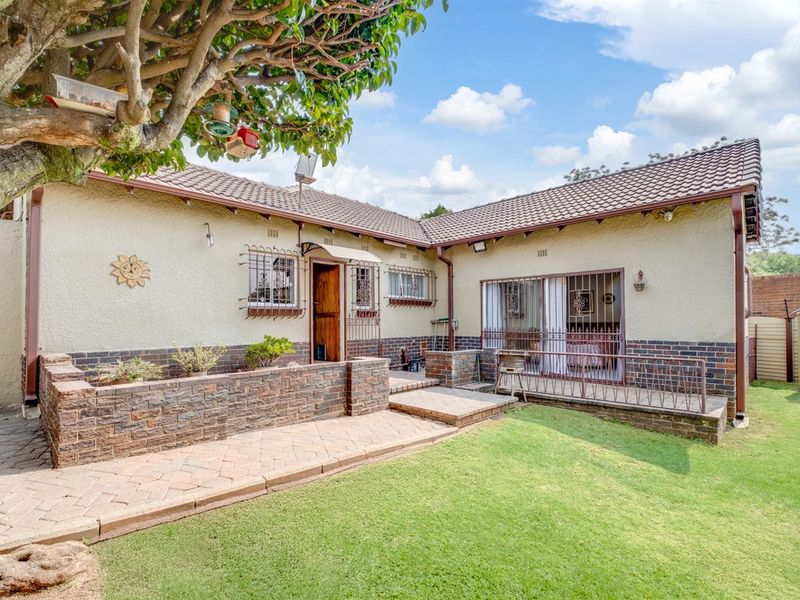 Rear view of the house featuring a paved patio area, brick retaining wall, well-maintained lawn, and secure sliding door access.