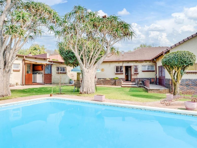 A backyard view featuring a swimming pool, established trees, and a brick-finished house exterior with security bars on the windows.