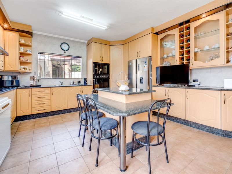 Spacious kitchen featuring light wood cabinetry, granite countertops, a central island with seating, and integrated appliances including an oven and microwave.