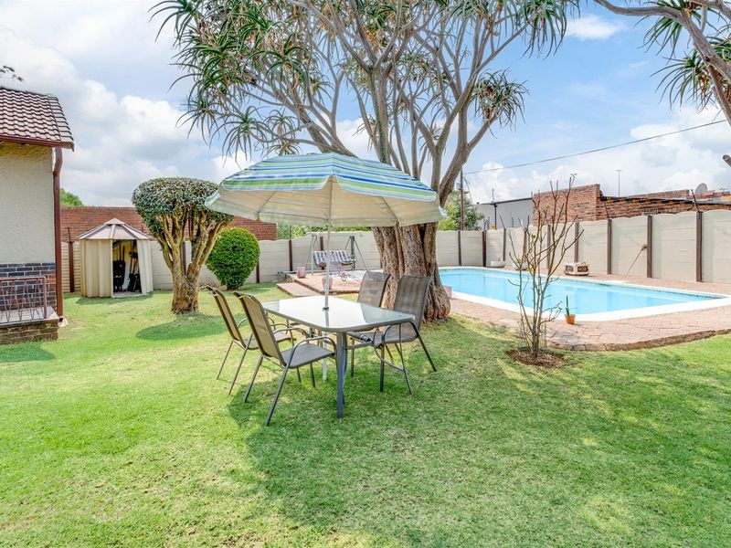 A private backyard featuring a swimming pool with paved surround, established trees, and a lawn area enclosed by a precast concrete boundary wall.