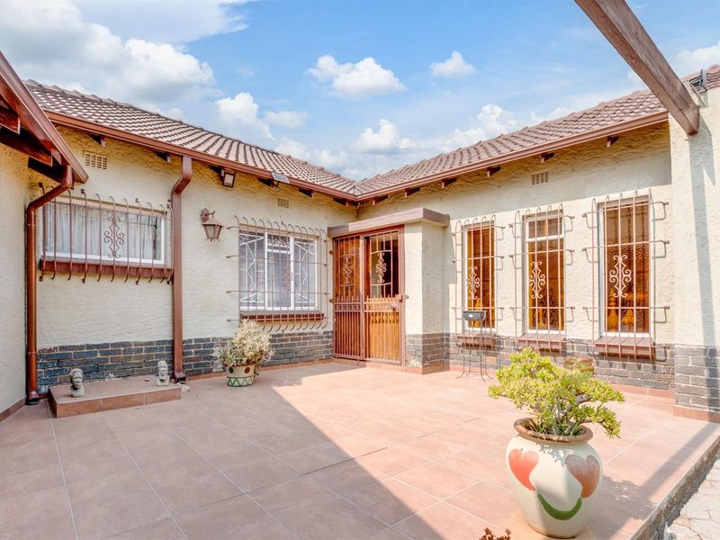 A paved outdoor patio area featuring a tiled floor, security bars on windows, and a secure entrance gate, ideal for outdoor living.