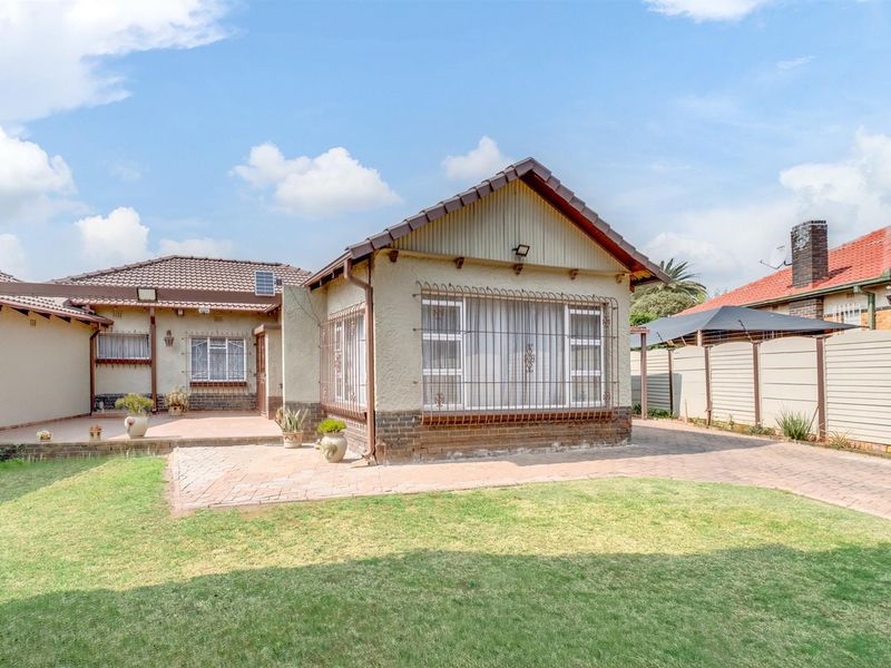 Rear view of the property featuring a paved patio area, lawn, and secure window treatments, showing a well-maintained exterior structure.