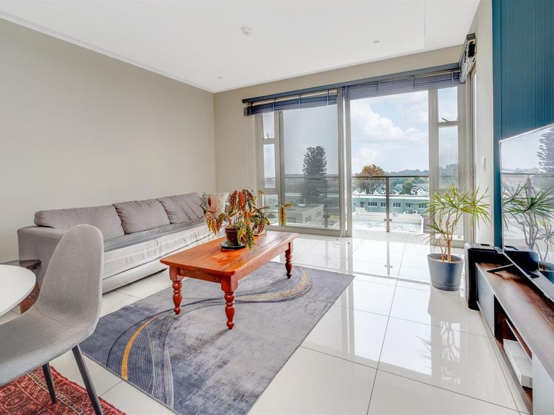 Bright living area featuring large sliding glass doors that open onto a balcony, with polished floor tiles and neutral wall finishes.