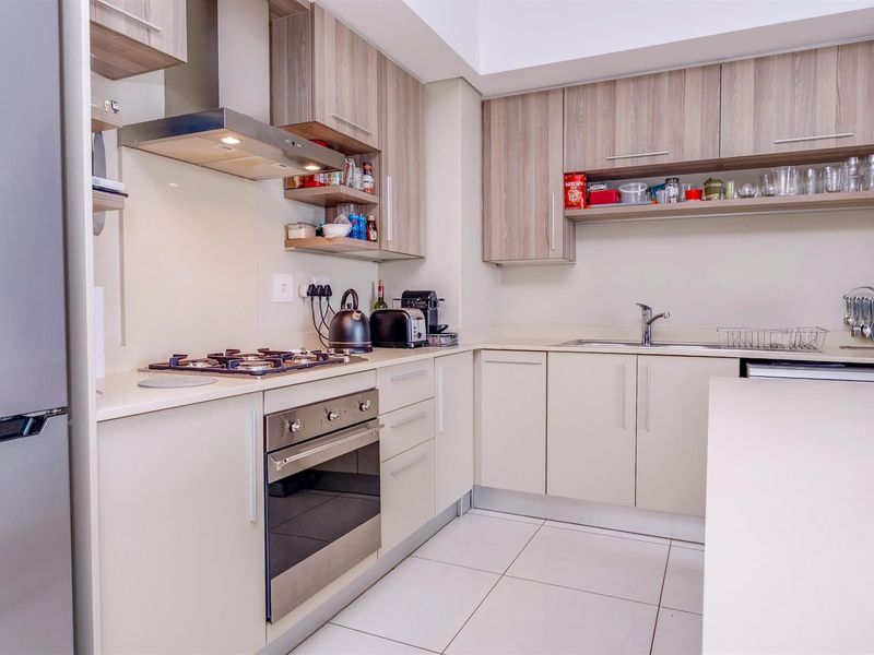 Modern kitchen featuring light wood-tone cabinetry, stone countertops, a built-in oven, gas hob, stainless steel extractor fan, and tiled flooring.