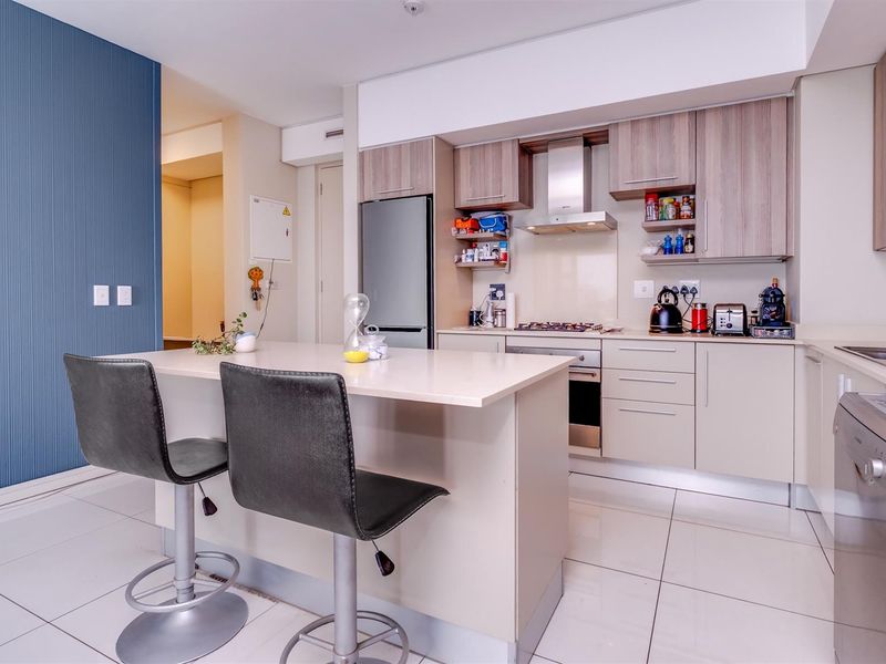 Modern open-plan kitchen featuring light-toned cabinetry, stone countertops, a breakfast island, and integrated stainless steel appliances.