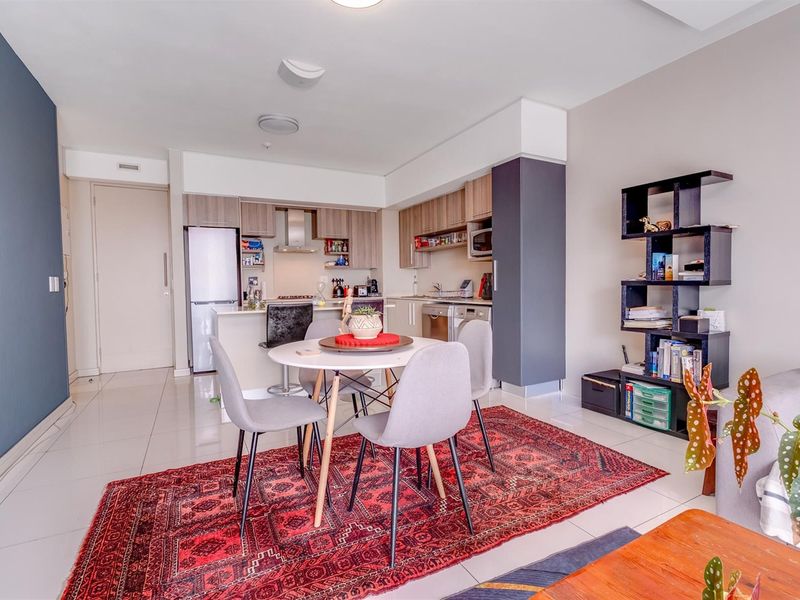 Open-plan living area featuring a modern kitchen with built-in cabinetry, integrated appliances, and tiled flooring, seamlessly flowing into the dining and lounge space.