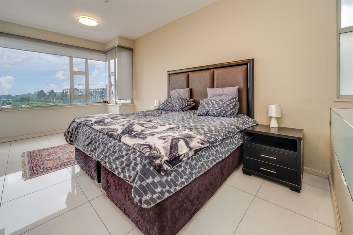 A bright bedroom featuring large windows with expansive views, neutral wall tones, and polished tile flooring.
