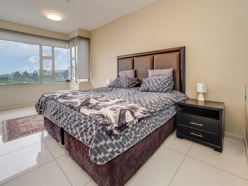 A bright bedroom featuring large windows with expansive views, neutral wall tones, and polished tile flooring.