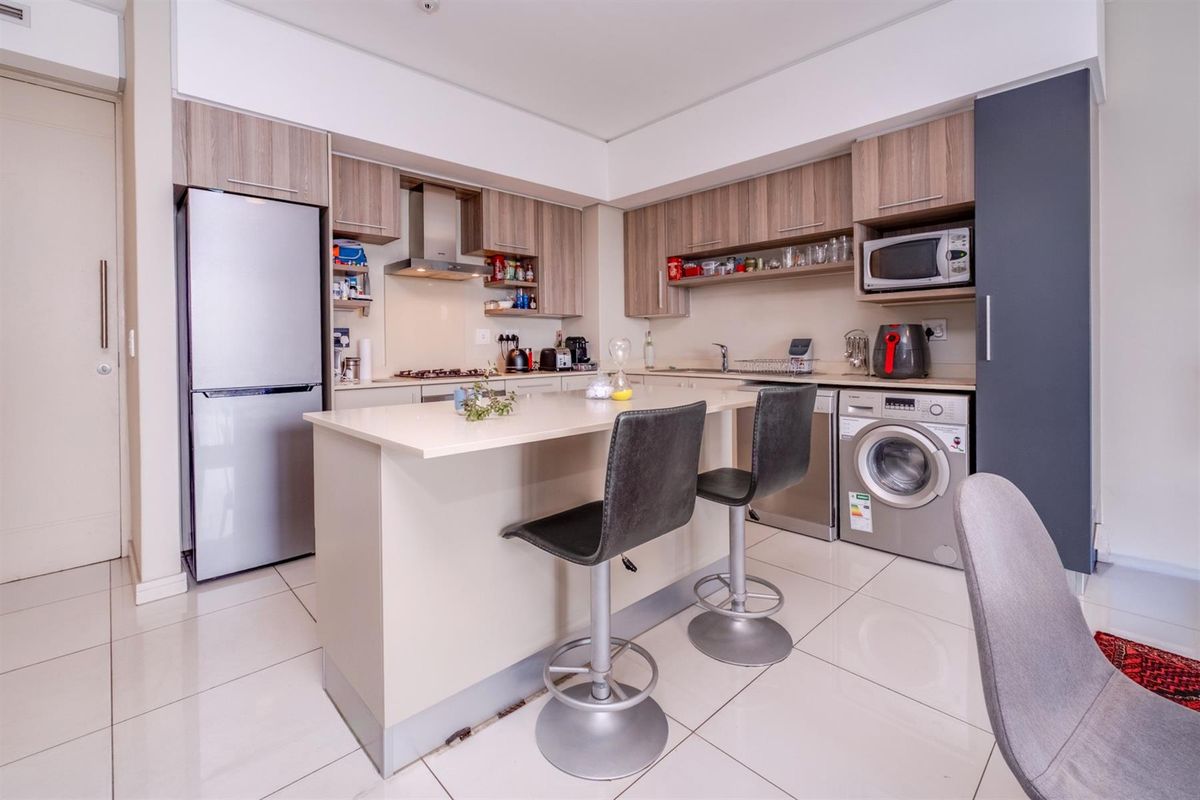 Modern open-plan kitchen featuring light wood cabinetry, stone countertops, a central breakfast island, and integrated appliances including a hob, oven, and extractor fan.