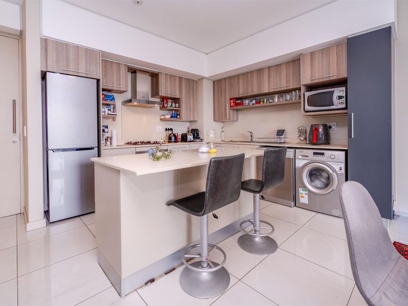 Modern open-plan kitchen featuring light wood cabinetry, stone countertops, a central breakfast island, and integrated appliances including a hob, oven, and extractor fan.