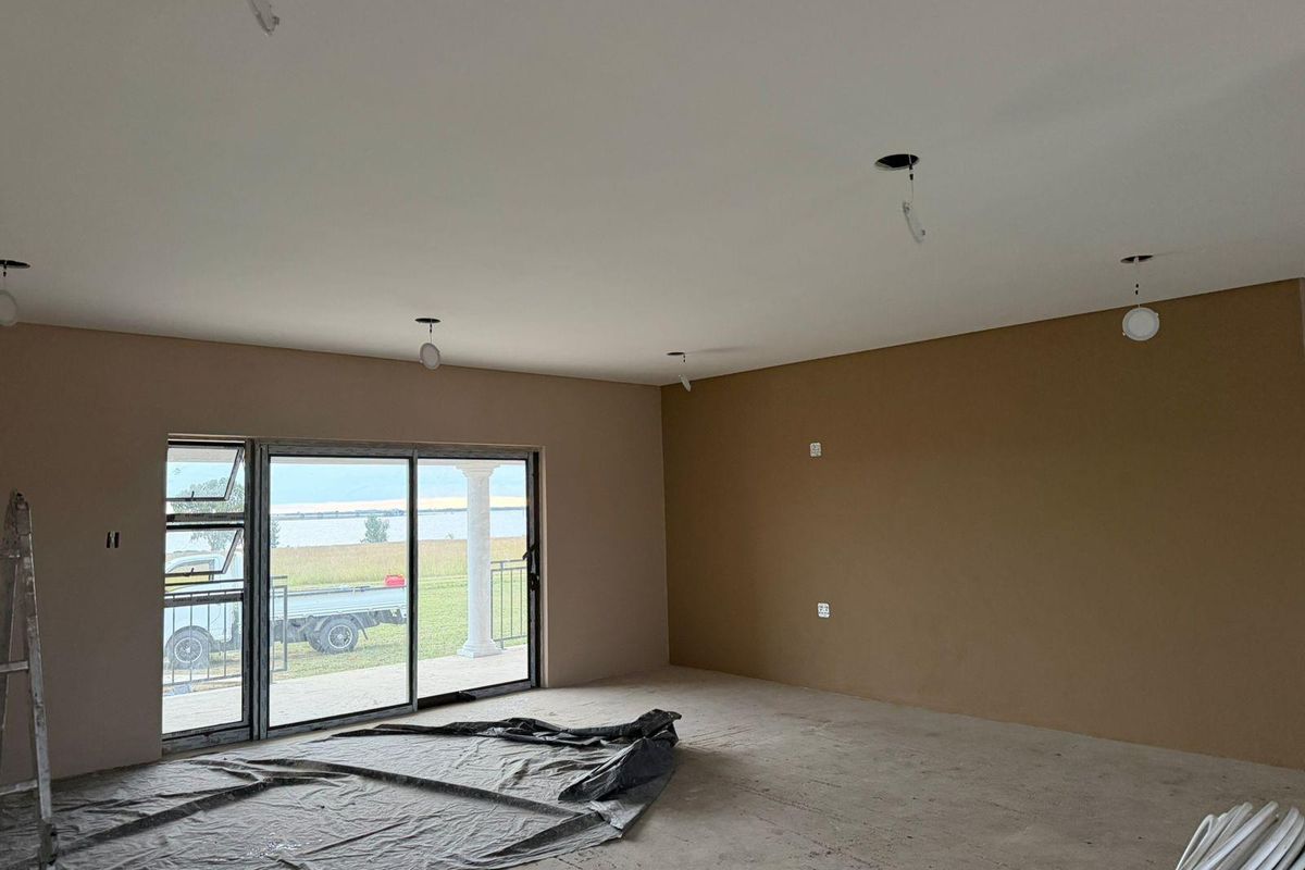 An unfinished living area featuring large sliding glass doors, neutral wall tones, and exposed electrical points, currently undergoing renovation.
