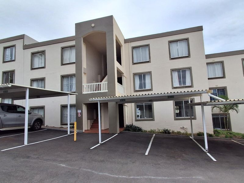 Exterior view of a multi-story apartment complex featuring covered parking bays and a paved driveway area.