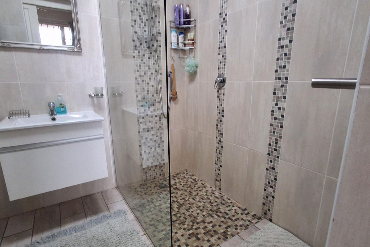 Modern bathroom featuring a walk-in shower with glass enclosure, mosaic tile accents, and a wall-mounted vanity basin.
