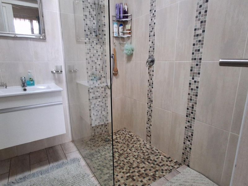 Modern bathroom featuring a walk-in shower with glass enclosure, mosaic tile accents, and a wall-mounted vanity basin.