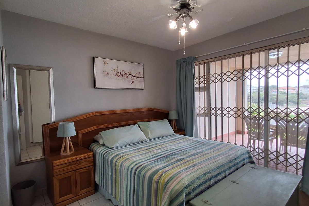 A bedroom featuring tiled flooring, a built-in wooden headboard, and a sliding glass door with a security gate leading to a balcony.