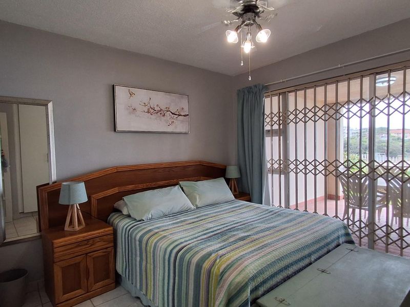 A bedroom featuring tiled flooring, a built-in wooden headboard, and a sliding glass door with a security gate leading to a balcony.