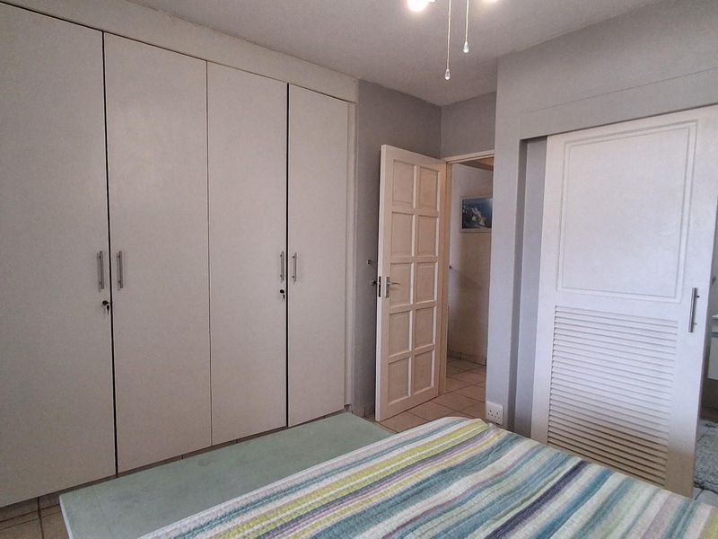 Bedroom featuring built-in floor-to-ceiling wardrobes, tiled flooring, and an en-suite bathroom with a wall-mounted vanity unit.