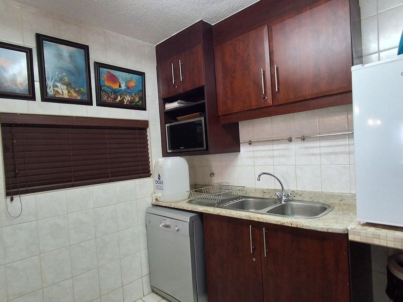 A functional kitchen featuring dark wood cabinetry, tiled walls, a double stainless steel sink, and granite-look countertops.