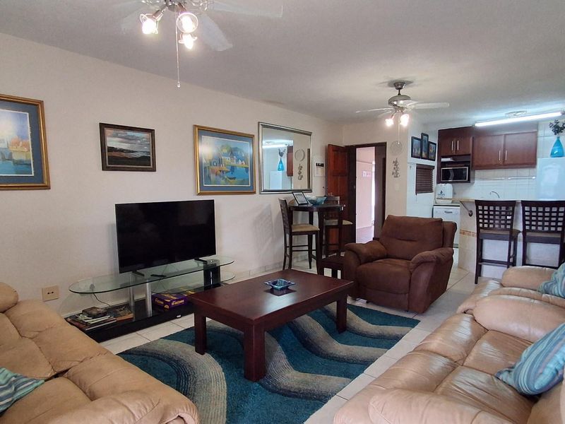 Open-plan living area featuring a kitchen with wooden cabinetry, breakfast bar, and tiled flooring, seamlessly connected to the lounge space.