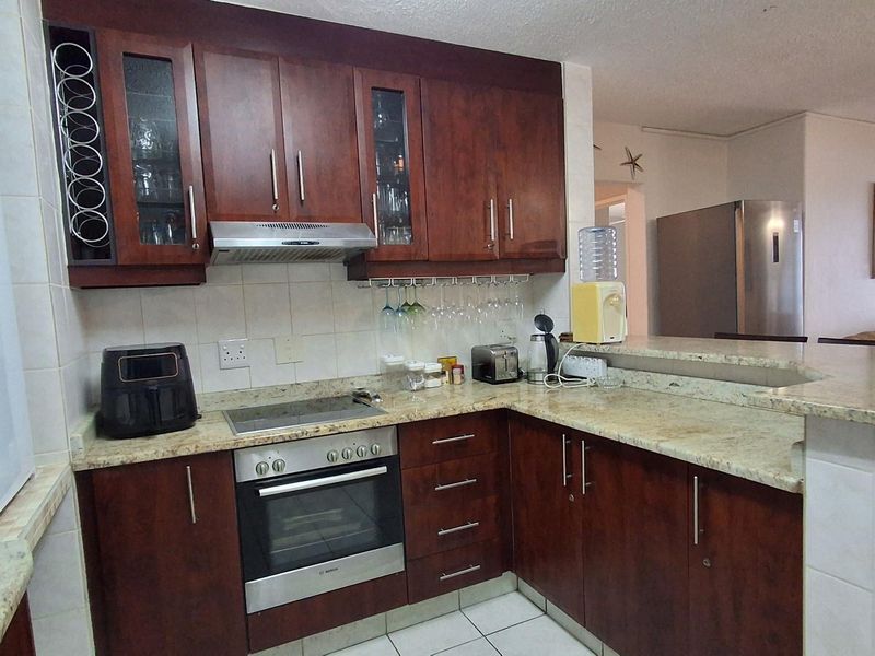 A functional kitchen featuring dark wood cabinetry, granite countertops, a built-in oven, and a breakfast bar overlooking the living area.