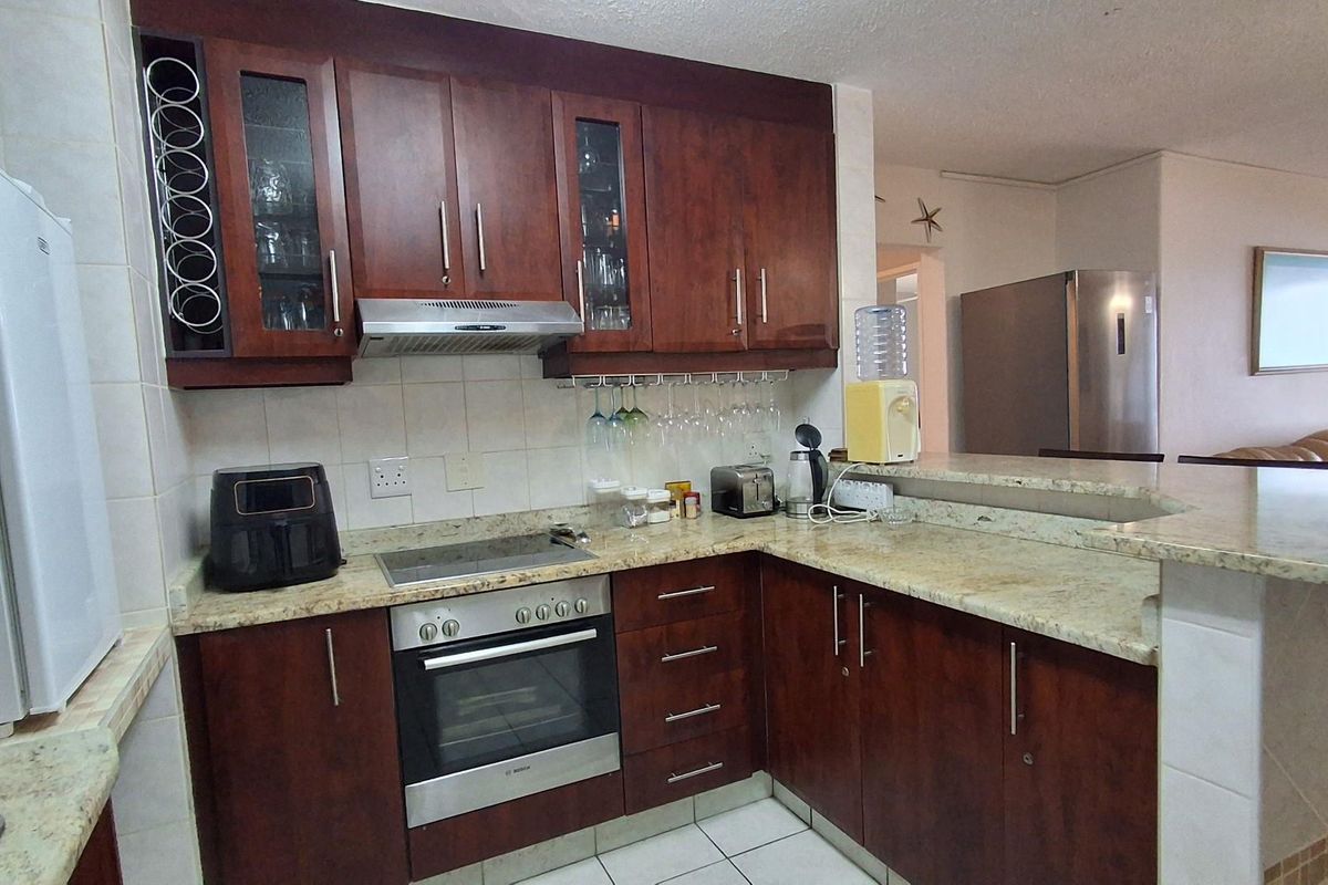 A functional kitchen featuring dark wood cabinetry, granite countertops, a built-in oven, and a breakfast bar overlooking the living area.