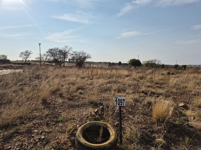 A vacant residential plot featuring natural dry grass, perimeter fencing, and a street light, ready for development.