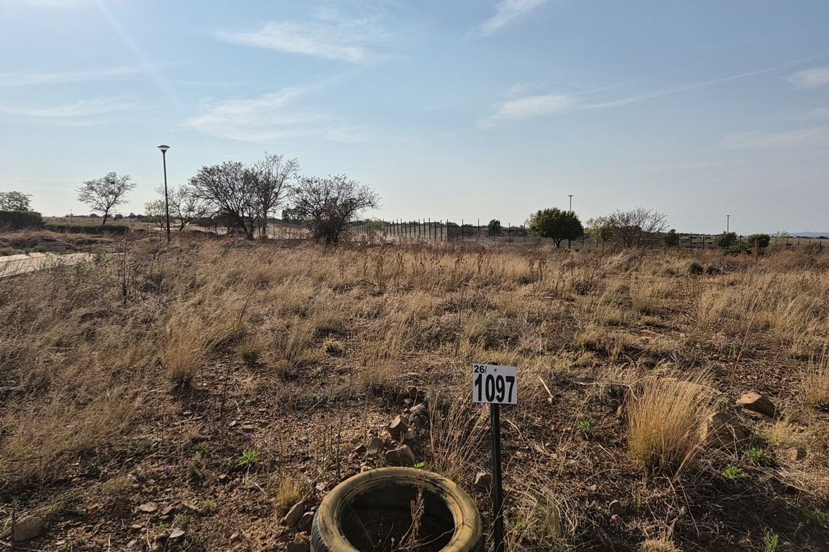 A vacant residential plot featuring natural dry grass, perimeter fencing, and a street light, ready for development.